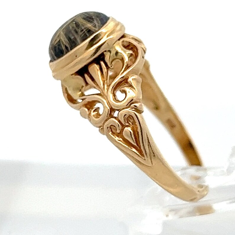 May include: A gold ring with an ornate design and a dark brown oval stone set in the center.