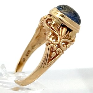 May include: A gold ring with a blue and white stone set in a bezel setting. The ring has a detailed, ornate design.