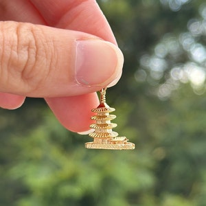 May include: A gold-colored pagoda charm pendant. The charm is detailed and intricate, with multiple tiers and a small base.