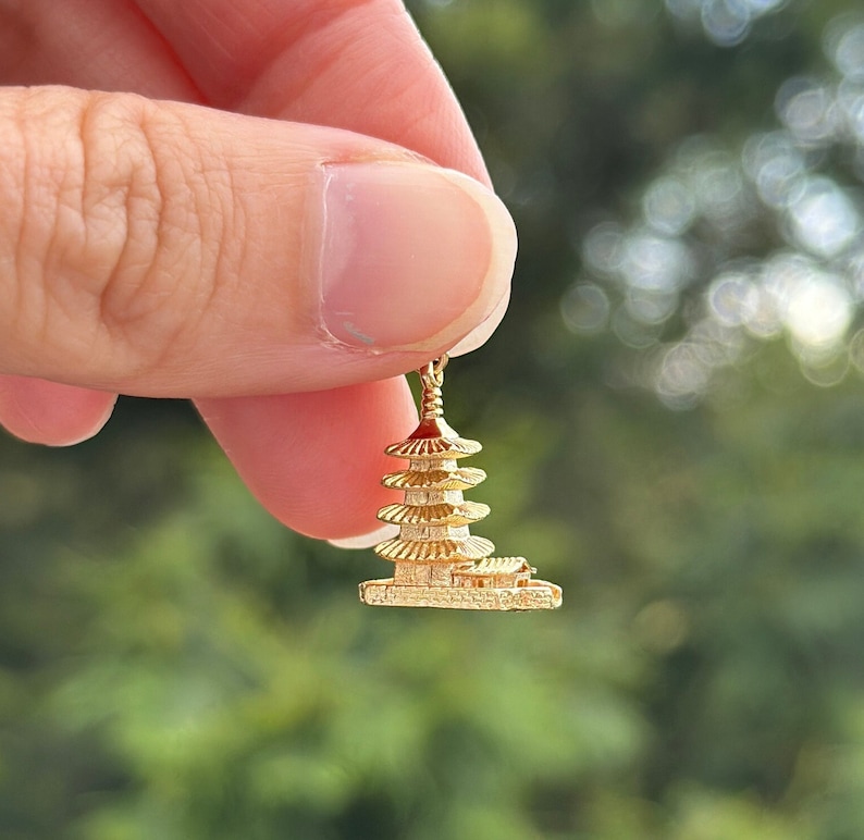 May include: A gold-colored pagoda charm pendant. The charm is detailed and intricate, with multiple tiers and a small base.