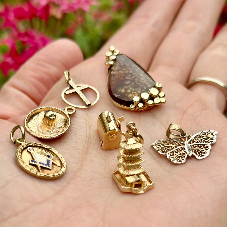 May include: A collection of gold charm pendants, including a cross, a sombrero, a mailbox, a pagoda, a butterfly, and a stone pendant.