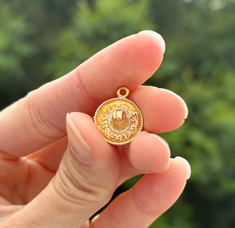 May include: A gold-colored charm in the shape of a sombrero. The charm has a detailed design and is perfect for adding a touch of Mexican flair to jewelry.