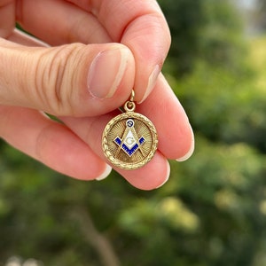 May include: A gold-colored pendant with a blue and white enamel Masonic symbol. The symbol is a compass and square with a 'G' in the center.