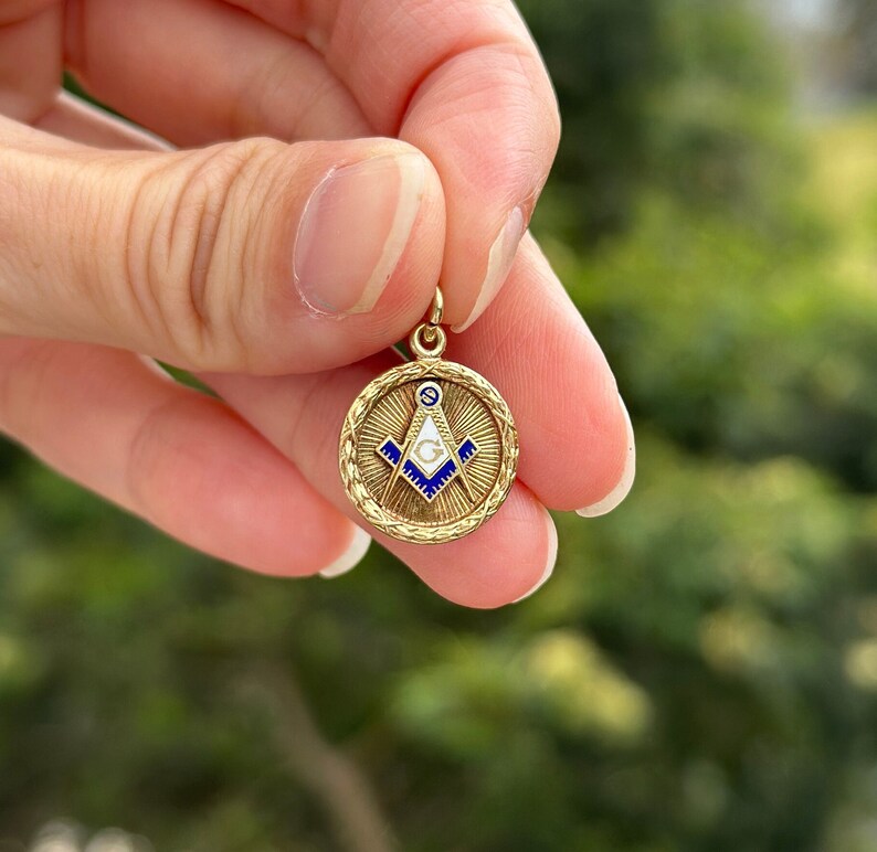 May include: A gold-colored pendant with a blue and white enamel Masonic symbol. The symbol is a compass and square with a 'G' in the center.