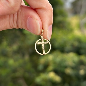 May include: A gold-toned cross pendant with a circle design. The cross is detailed with a textured pattern.