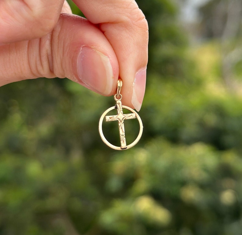 May include: A gold-toned cross pendant with a circle design. The cross is detailed with a textured pattern.