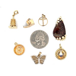 May include: A collection of seven gold charm pendants, including a pagoda, a butterfly, a compass, a cross, a small box, a sombrero, and a teardrop-shaped pendant with a brown and white agate stone.