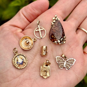 May include: A collection of gold-toned pendants, including a cross, a sombrero, a butterfly, a geometric design, and a stone pendant with a brown and gold pattern.