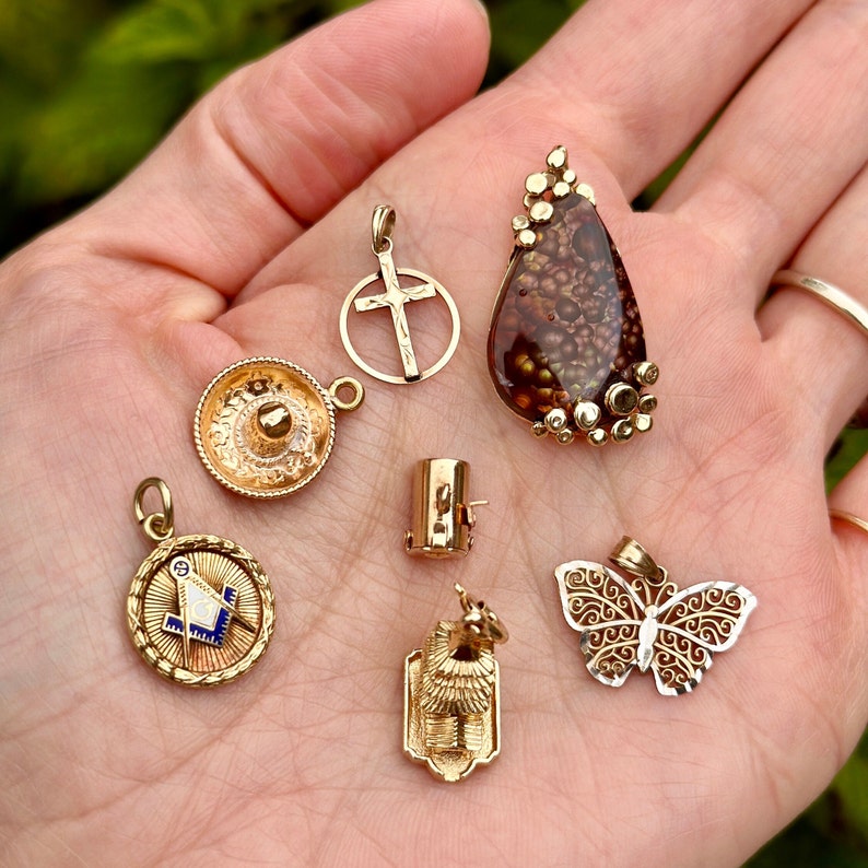 May include: A collection of gold-toned pendants, including a cross, a sombrero, a butterfly, a geometric design, and a stone pendant with a brown and gold pattern.