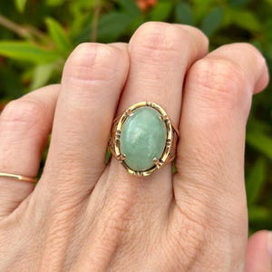 May include: A gold ring with a large oval green jade stone set in a decorative gold frame.