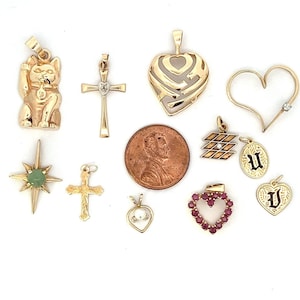 May include: A collection of 12 gold pendants, including a heart, a cross, a star, a cat, a letter U, and a heart with red stones. The pendants are arranged on a white surface with a penny for scale.