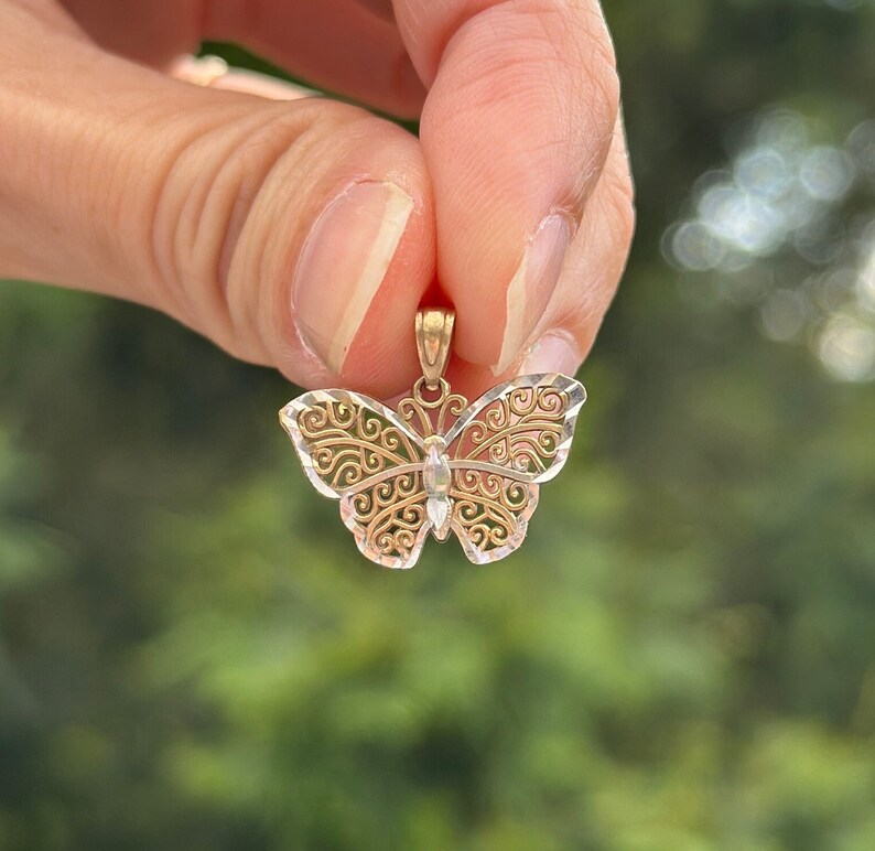 May include: A delicate gold butterfly pendant with intricate filigree details. The pendant is made of two-toned gold, with a yellow gold body and white gold accents.