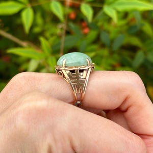 May include: A gold ring with a green jade stone set in a filigree design. The ring features a Chinese character for "double happiness" on the band.