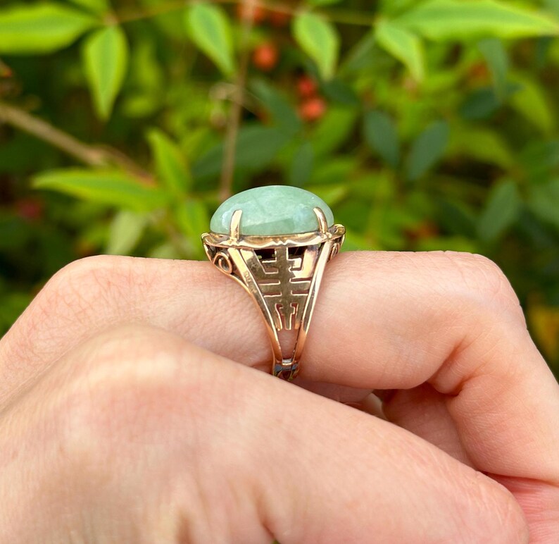 May include: A gold ring with a green jade stone set in a filigree design. The ring features a Chinese character for "double happiness" on the band.