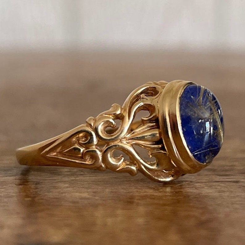 May include: A gold ring with an ornate filigree design and a blue oval stone set in the center.