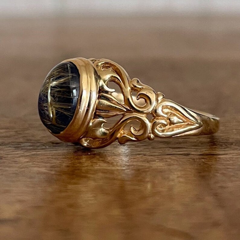 May include: A gold ring with an ornate design and a large, round, dark gemstone set in the center.