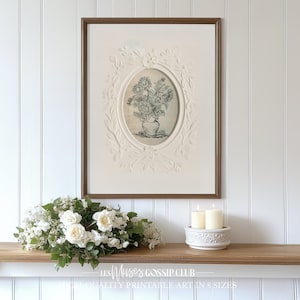 Peut inclure: Un dessin en noir et blanc encadré d'un bouquet de tournesols dans un vase. Le cadre est blanc avec un motif orné et une bordure dorée. Le dessin est affiché sur un mur blanc avec une étagère en bois blanc en dessous. L'étagère a un bougeoir blanc avec deux bougies blanches et une guirlande florale blanche.