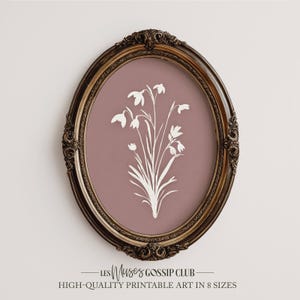 Peut inclure: Une impression encadrée ovale avec un motif floral blanc sur un fond mauve. Le cadre orné, marron foncé, entoure l'œuvre d'art. Le texte en bas indique "LES Muses GOSSIP CLUB" et "HIGH-QUALITY PRINTABLE ART IN 8 SIZES."