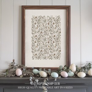 Peut inclure: Une impression encadrée avec un motif de feuilles et de fleurs brunes et dorées sur fond blanc. L'impression est accrochée à un mur blanc au-dessus d'une cheminée décorée de branches d'eucalyptus et d'œufs de Pâques mouchetés.