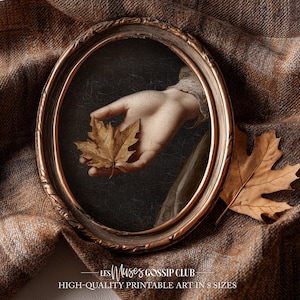 Peut inclure: Un cadre ovale de couleur bronze entoure une main tenant une feuille brun doré. L'arrière-plan présente un tissu brun texturé. Le texte "LES Muses GOSSIP CLUB" et "HIGH-QUALITY PRINTABLE ART IN 8 SIZES" est en bas.