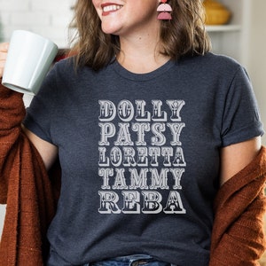May include: A dark blue t-shirt with white text that reads "DOLLY PATSY LORETTA TAMMY REBA".