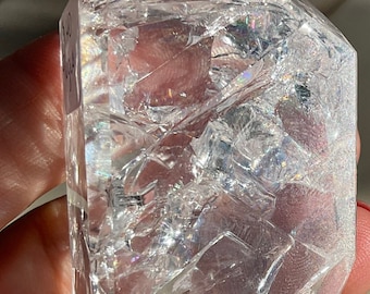May include: A clear quartz crystal with a unique, faceted shape. The crystal is smooth and polished, with a slight iridescent sheen.