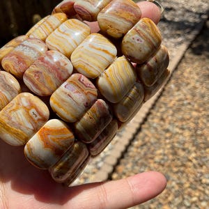 May include: A bracelet made of stacked, square-shaped, polished, banded agate beads in shades of brown, orange, white, and red.