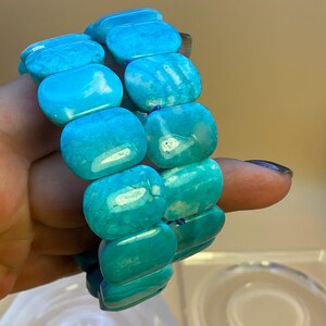 May include: A stretch bracelet composed of smooth, rectangular, bright turquoise blue beads. The beads feature natural-looking white veining and a polished finish, strung together to form a continuous loop that fits around the wrist.
