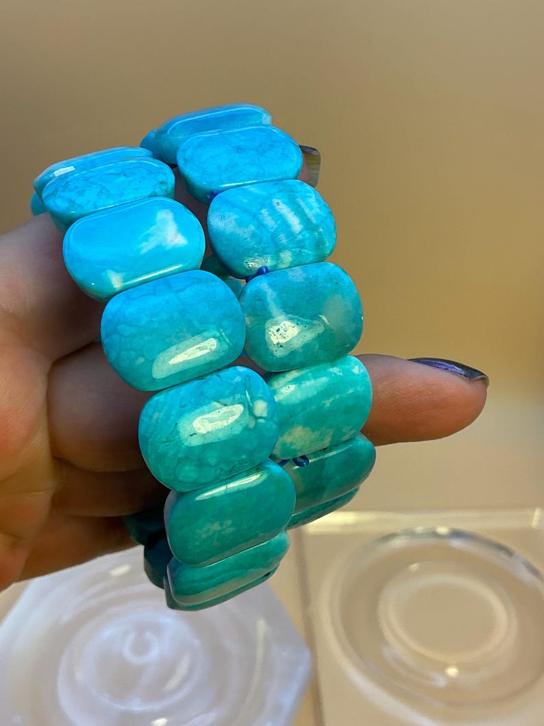May include: A stretch bracelet composed of smooth, rectangular, bright turquoise blue beads. The beads feature natural-looking white veining and a polished finish, strung together to form a continuous loop that fits around the wrist.
