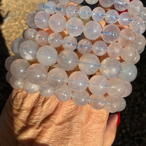 May include: A stack of clear quartz crystal bracelets with a frosted finish. The bracelets are made of round beads and are stacked on top of each other.
