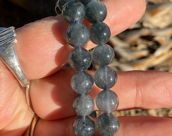 Könnte beinhalten: Zwei Armbänder aus dunkelgrauen, runden Edelsteinperlen. Die Perlen sind durchscheinend und scheinen schwarze Einschlüsse zu haben.