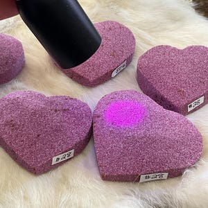 May include: Four heart-shaped pink sanding stones with numbers #28, #28, #28, and #48 printed on them. The stones are on a white furry surface.