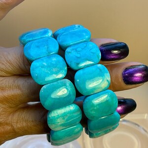 May include: Two stretch bracelets composed of smooth, rectangular turquoise-colored beads. Each bead features natural white veining and a polished finish. The bracelets are strung on an elastic cord, allowing them to expand and fit comfortably.