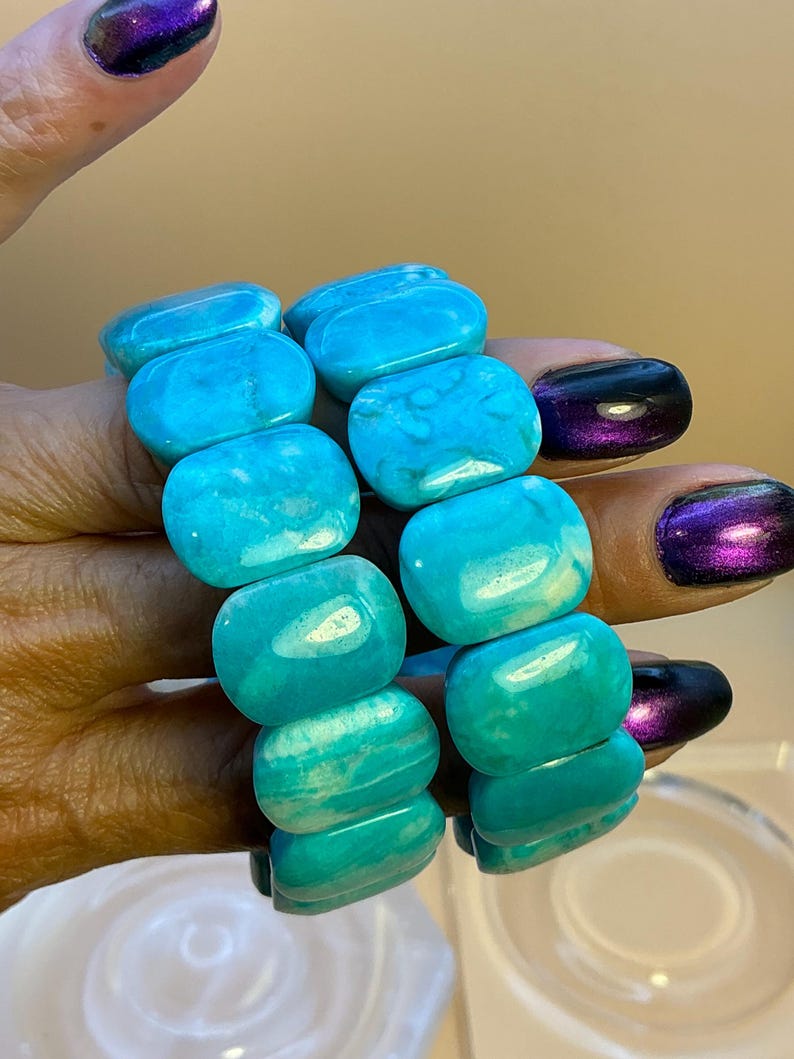 May include: Two stretch bracelets composed of smooth, rectangular turquoise-colored beads. Each bead features natural white veining and a polished finish. The bracelets are strung on an elastic cord, allowing them to expand and fit comfortably.
