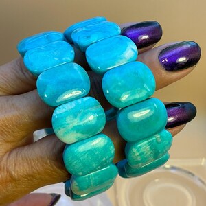 May include: A stretch bracelet composed of smooth, rectangular turquoise-colored beads with natural white marbling patterns. The beads are polished to a glossy finish and strung together in a continuous loop to form a flexible wrist accessory.