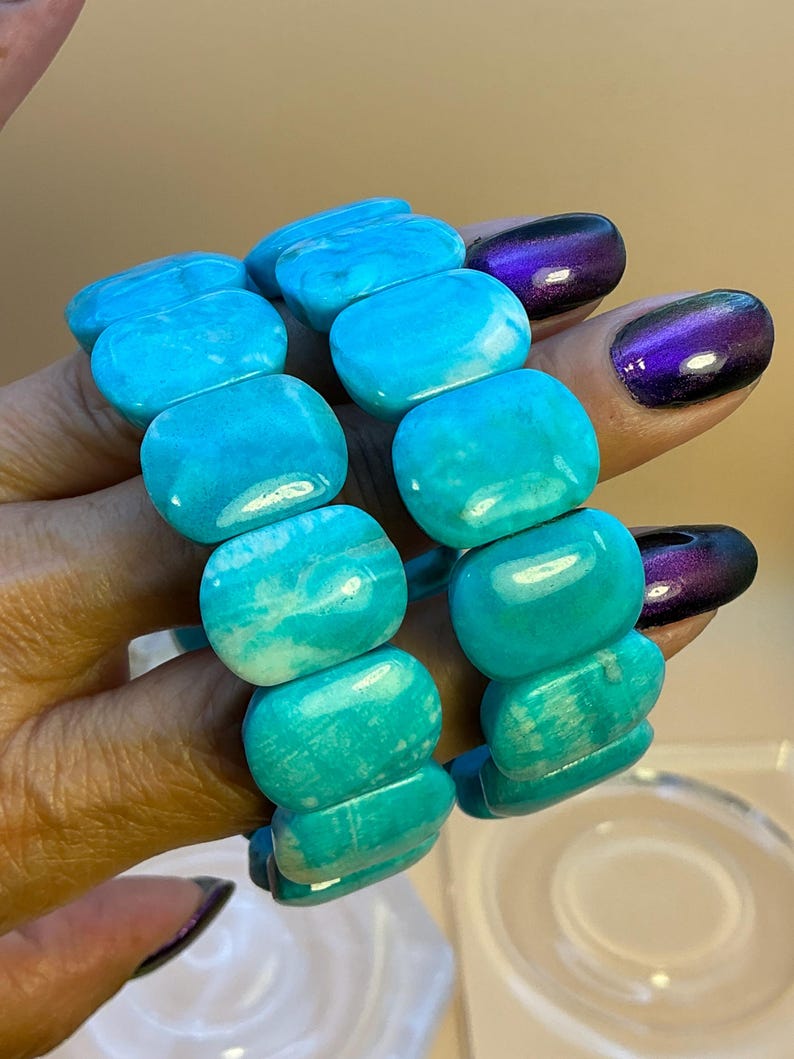 May include: A stretch bracelet composed of smooth, rectangular turquoise-colored beads with natural white marbling patterns. The beads are polished to a glossy finish and strung together in a continuous loop to form a flexible wrist accessory.