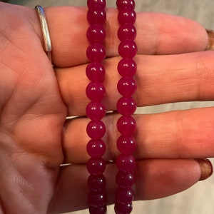 May include: Two red beaded bracelets with round beads. The bracelets are made of a smooth, shiny material.