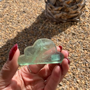 May include: A green fluorite crystal carved into the shape of a cloud. The crystal is translucent and has a light green color.