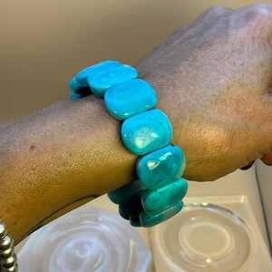 May include: A stretch bracelet composed of multiple smooth, rectangular turquoise-colored beads with a polished finish. The beads are arranged in a single row, creating a continuous loop that fits around the wrist, showcasing a vibrant blue-green hue.