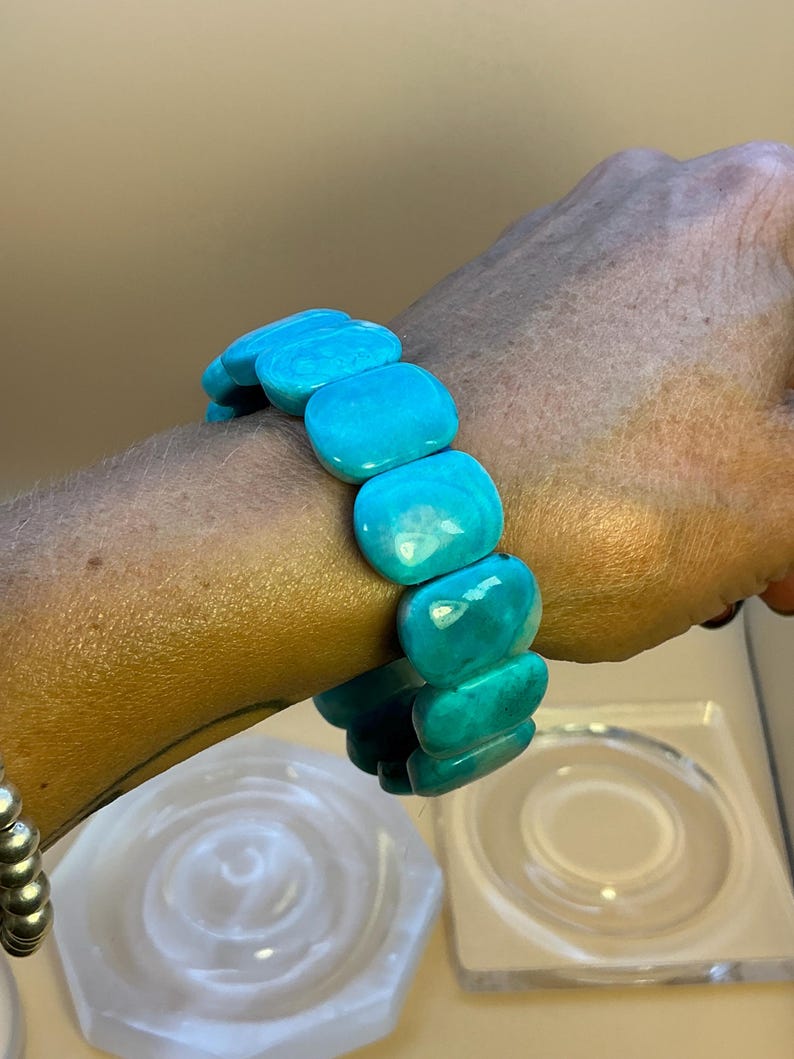 May include: A stretch bracelet composed of multiple smooth, rectangular turquoise-colored beads with a polished finish. The beads are arranged in a single row, creating a continuous loop that fits around the wrist, showcasing a vibrant blue-green hue.