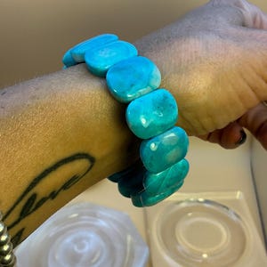 May include: A stretch bracelet composed of smooth, polished, rectangular turquoise-colored beads. The beads feature variations in blue and teal tones with subtle white marbling throughout, arranged in a single strand that encircles the wrist.