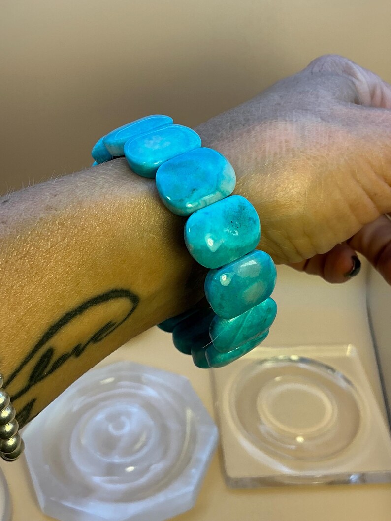 May include: A stretch bracelet composed of smooth, polished, rectangular turquoise-colored beads. The beads feature variations in blue and teal tones with subtle white marbling throughout, arranged in a single strand that encircles the wrist.