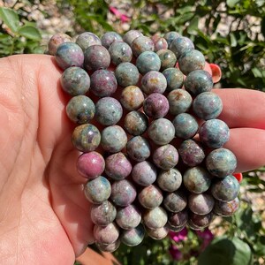 Könnte beinhalten: Ein Stapel Armbänder aus runden, mehrfarbigen, grünen, rosa und braunen Edelsteinperlen.