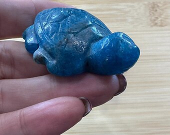May include: A small, blue turtle figurine carved from stone. The turtle has detailed features, including a textured shell and visible limbs. The figurine is a vibrant shade of blue and appears to be a decorative item.