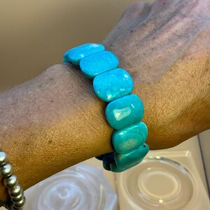 May include: A stretch bracelet composed of smooth, rectangular turquoise-colored beads with natural marbling. The beads are arranged in a single row, featuring a vibrant cyan hue with subtle white and darker blue veining throughout the polished surface.