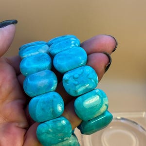 May include: Two bracelets composed of smooth, polished, rectangular turquoise-colored beads. The beads feature natural variations in shade, ranging from bright cyan to deeper blue tones, with subtle white marbling throughout the stone surfaces.