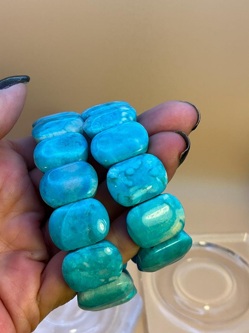 May include: Two bracelets composed of smooth, polished, rectangular turquoise-colored beads. The beads feature natural variations in shade, ranging from bright cyan to deeper blue tones, with subtle white marbling throughout the stone surfaces.