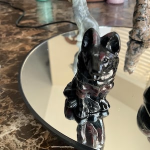 May include: Black obsidian dog figurine with red accents sitting on a mirrored surface.