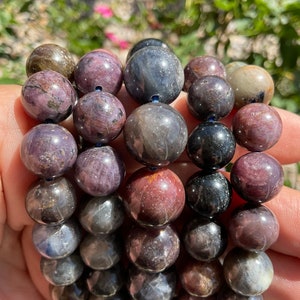 Puede incluir: Un brazalete de múltiples hilos hecho con cuentas redondas de piedras preciosas de color azul oscuro, morado y marrón.