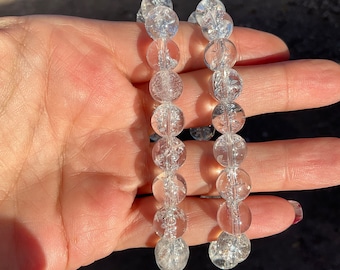 May include: Two clear crystal bracelets with small, round beads. The bracelets are made of clear quartz crystals with a slightly cloudy appearance.